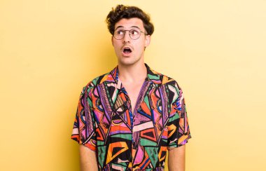 Genç yakışıklı adam şok olmuş, mutlu, şaşkın ve şaşırmış hissediyor, ağzı açık bir şekilde yana bakıyor.