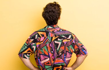 Genç, yakışıklı bir adam kafası karışık ya da dolu ya da şüphe ve soru dolu, merak ediyor, elleri kalçasında, dikiz aynasından.