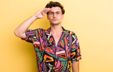 Genç ve yakışıklı bir adam saygı göstererek, onur ve vatanseverlik adına askeri bir selamla kamerayı selamlıyor.