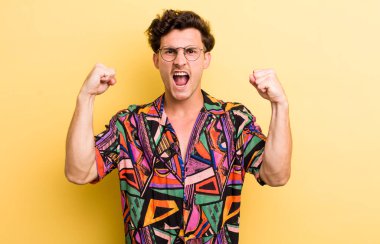 Genç yakışıklı bir adam sinirli bir ifadeyle ya da yumruklarıyla başarıyı kutlarken agresif bir şekilde bağırıyor.