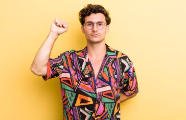 Genç yakışıklı adam ciddi, güçlü ve asi hissediyor, yumruğunu kaldırıyor, protesto ediyor ya da devrim için savaşıyor.