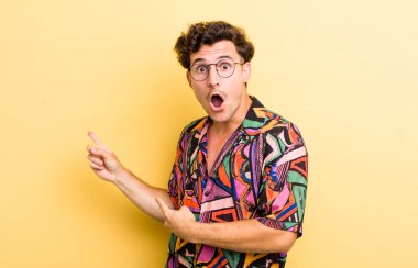 Genç yakışıklı adam şaşkın ve şaşırmış hissediyor. Kenardaki fotokopi alanını işaret ediyor. Şaşırmış, ağzı açık bir bakış.