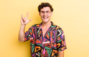 Genç yakışıklı adam kendini mutlu, eğlenceli, kendinden emin, pozitif ve asi hissediyor, elle rock ya da heavy metal işareti yapıyor.