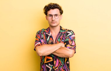 Genç yakışıklı adam hayal kırıklığına uğramış ve hayal kırıklığına uğramış, ciddi görünüyor, kızgın ve kollarını kavuşturmuş.