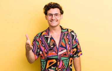 Genç yakışıklı adam gülümsüyor, mutlu görünüyor, kendinden emin ve arkadaş canlısı, bir anlaşmaya varmak için el sıkışıyor, işbirliği yapıyor.