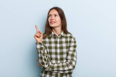 Genç ve güzel bir kadın mutlu bir şekilde gülümsüyor ve yan bakıyor, merak ediyor, düşünüyor ya da bir fikri var.