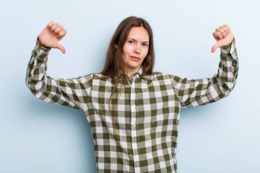 Genç ve güzel bir kadın üzgün, hayal kırıklığına uğramış ya da kızgın görünüyor. Anlaşmazlık içinde başparmaklarını gösteriyor. Hayal kırıklığına uğramış hissediyor.