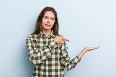 Genç ve güzel bir kadın gülümsüyor, mutlu, kaygısız ve tatmin olmuş hissediyor, fotokopi alanındaki konsepte veya fikre işaret ediyor.