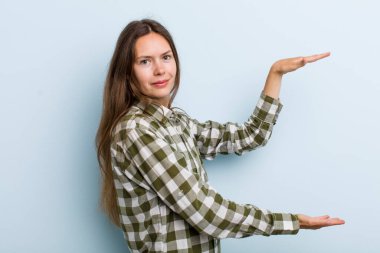 Genç ve güzel bir kadın gülümsüyor, mutlu, pozitif ve tatmin olmuş hissediyor, fotokopi alanında nesne ya da konsept tutuyor ya da gösteriyor