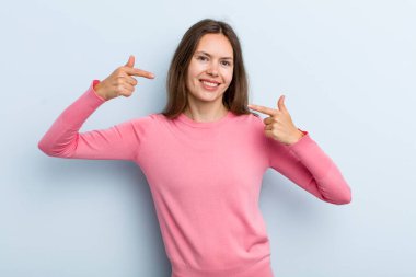 Genç ve güzel bir kadın, kendine güvenerek gülümsüyor. Kendi gülüşünü gösteriyor. Olumlu, rahat, tatmin olmuş bir tavır.