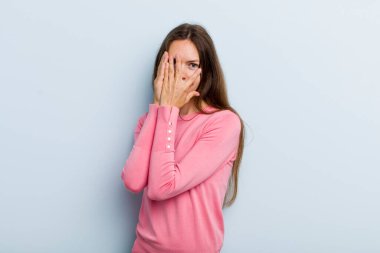 young adult pretty woman feeling scared or embarrassed, peeking or spying with eyes half-covered with hands