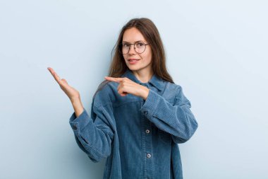 Genç ve güzel bir kadın neşeyle gülümsüyor ve yan taraftaki fotokopi alanını işaret ediyor, bir nesneyi gösteriyor ya da reklamını yapıyor.