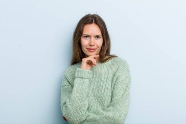 Genç ve güzel bir kadın mutlu görünüyor ve eli çenesinde gülümsüyor, merak ediyor ya da soru soruyor, seçenekleri karşılaştırıyor.