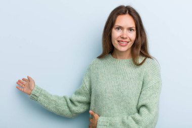 young adult pretty woman feeling happy and cheerful, smiling and welcoming you, inviting you in with a friendly gesture