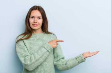 Genç ve güzel bir kadın gülümsüyor, mutlu, kaygısız ve tatmin olmuş hissediyor, fotokopi alanındaki konsepte veya fikre işaret ediyor.