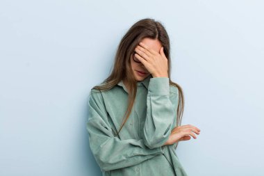 Genç ve güzel bir kadın stresli, utanmış ya da üzgün görünüyor, baş ağrısı var, yüzünü eliyle kapatıyor.