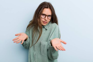 young adult pretty woman feeling clueless and confused, having no idea, absolutely puzzled with a dumb or foolish look