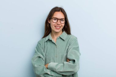 Genç ve güzel bir kadın mutlu, gururlu ve memnun görünüyor. Kollarını kavuşturup gülümsüyor.