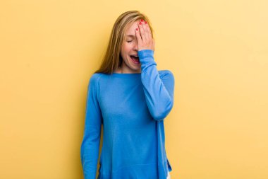 young adult blonde pretty woman laughing and slapping forehead like saying doh! I forgot or that was a stupid mistake 