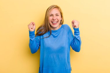 Genç, sarışın, güzel bir kadın mutlu, şaşırmış ve gururlu, bağırıyor ve başarıyı büyük bir gülümsemeyle kutluyor.