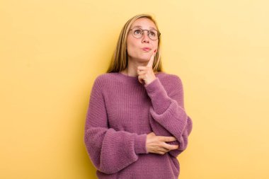 Genç, sarışın, güzel bir kadın. Yoğunlaşmış bakışları var. Şüpheli bir ifadeyle yukarı ve yana bakıyor.