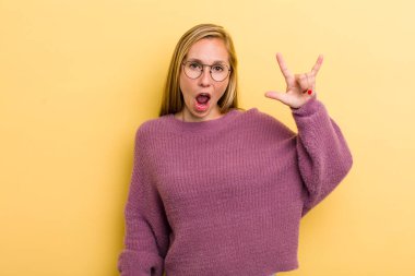 Genç, sarışın, güzel bir kadın kendini mutlu, eğlenceli, kendinden emin, pozitif ve asi hissediyor, elle rock veya heavy metal işareti yapıyor.