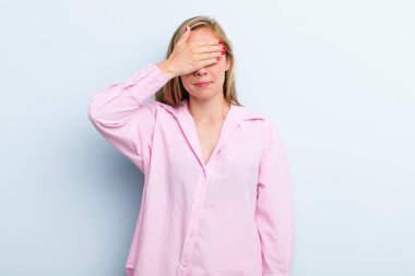 Genç, sarışın, güzel bir kadın tek eliyle gözlerini kapatıyor. Korkmuş ya da endişeli, merak ediyor ya da körü körüne bir sürpriz bekliyor.