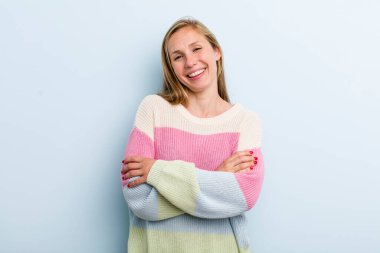 young adult blonde pretty woman laughing happily with arms crossed, with a relaxed, positive and satisfied pose