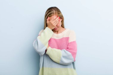 young adult blonde pretty woman looking stressed, ashamed or upset, with a headache, covering face with hand