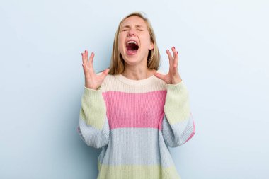 Genç, sarışın, güzel bir kadın öfkeyle bağırıyor, stresli ve elleri havada, neden ben diye bağırıyor.