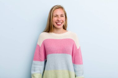 young adult blonde pretty woman looking happy and friendly, smiling and winking an eye at you with a positive attitude