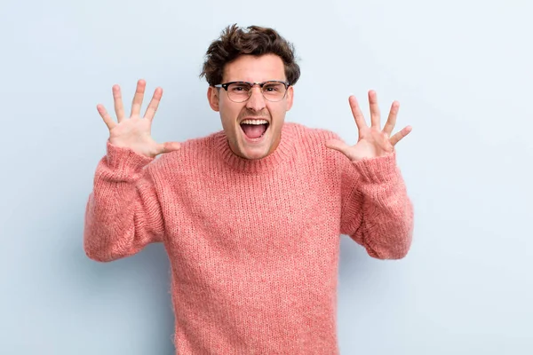 Genç ve yakışıklı bir adam panik ya da öfke içinde bağırıyor, şok olmuş, korkmuş ya da öfkeli, elleri başının yanında.