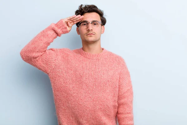 Genç ve yakışıklı bir adam saygı göstererek, onur ve vatanseverlik adına askeri bir selamla kamerayı selamlıyor.