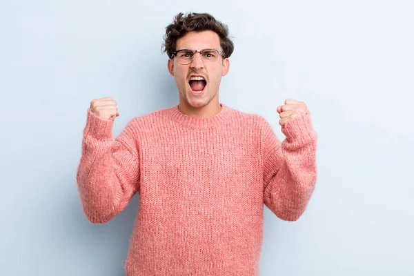 Genç yakışıklı bir adam sinirli bir ifadeyle ya da yumruklarıyla başarıyı kutlarken agresif bir şekilde bağırıyor.