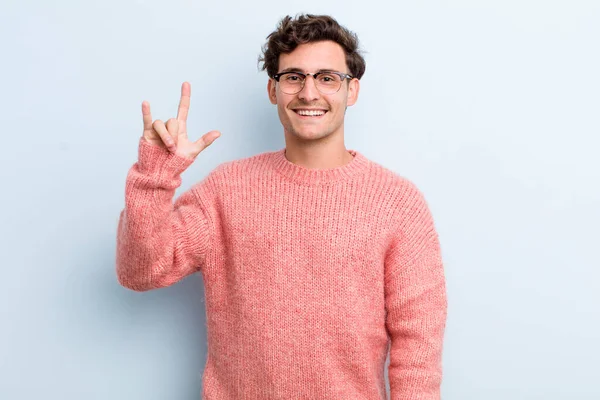 Genç yakışıklı adam kendini mutlu, eğlenceli, kendinden emin, pozitif ve asi hissediyor, elle rock ya da heavy metal işareti yapıyor.