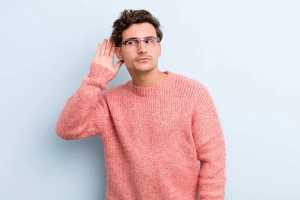 Genç yakışıklı adam ciddi ve meraklı görünüyor, dinliyor, gizli bir konuşma veya dedikodu duymaya çalışıyor, kulak misafiri oluyor.