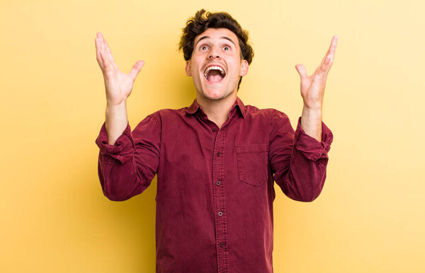 Молодой красивый мужчина чувствует себя счастливым, изумленным, счастливым и удивленным, празднуя победу с поднятыми руками