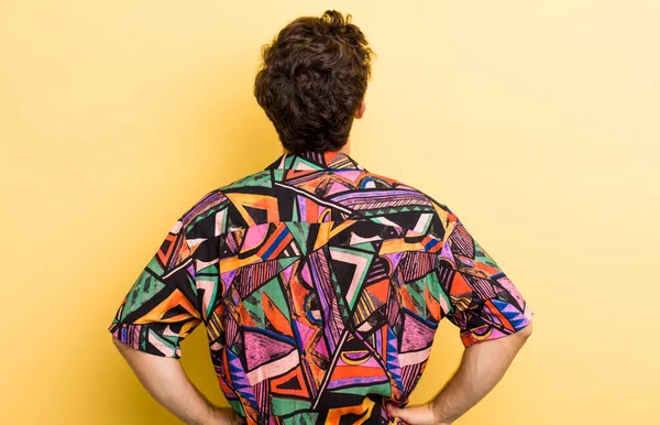 Genç, yakışıklı bir adam kafası karışık ya da dolu ya da şüphe ve soru dolu, merak ediyor, elleri kalçasında, dikiz aynasından.