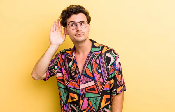 Genç yakışıklı adam ciddi ve meraklı görünüyor, dinliyor, gizli bir konuşma veya dedikodu duymaya çalışıyor, kulak misafiri oluyor.