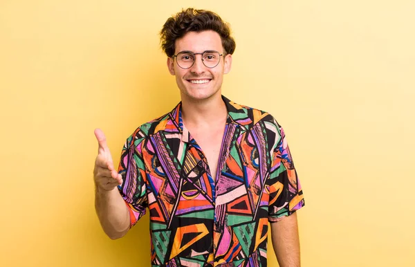 Genç yakışıklı adam gülümsüyor, mutlu görünüyor, kendinden emin ve arkadaş canlısı, bir anlaşmaya varmak için el sıkışıyor, işbirliği yapıyor.