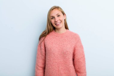 young adult blonde pretty woman smiling cheerfully and casually with a positive, happy, confident and relaxed expression