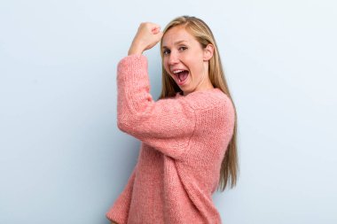 Genç, sarışın, güzel bir kadın kendini mutlu, tatmin olmuş ve güçlü hissediyor, kaslı ve formda, spor salonundan sonra güçlü görünüyor.