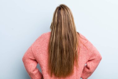 young adult blonde pretty woman feeling confused or full or doubts and questions, wondering, with hands on hips, rear view