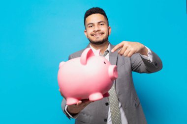 hispanic businessman pointing or showing and holding a piggy bank