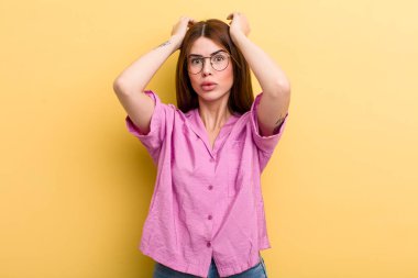 young adult pretty woman looking excited and surprised, open-mouthed with both hands on head, feeling like a lucky winner