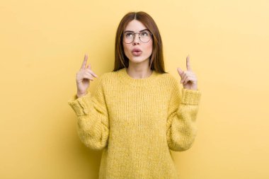 young adult pretty woman feeling awed and open mouthed pointing upwards with a shocked and surprised look