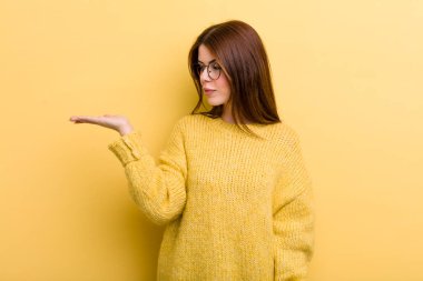 young adult pretty woman feeling happy and smiling casually, looking to an object or concept held on the hand on the side