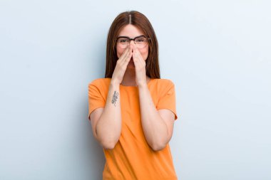 young adult pretty woman looking happy, cheerful, lucky and surprised covering mouth with both hands