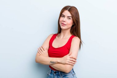 Genç ve güzel bir kadın kollarını kavuşturup mutlu bir şekilde gülüyor, rahat, pozitif ve tatmin edici bir pozla.