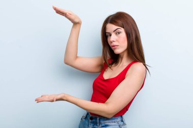 Genç ve güzel bir kadın iki eli de kenarda duran bir objeyi tutuyor, fotokopi alanında, bir nesneyi gösteriyor, sunuyor ya da reklamını yapıyor.